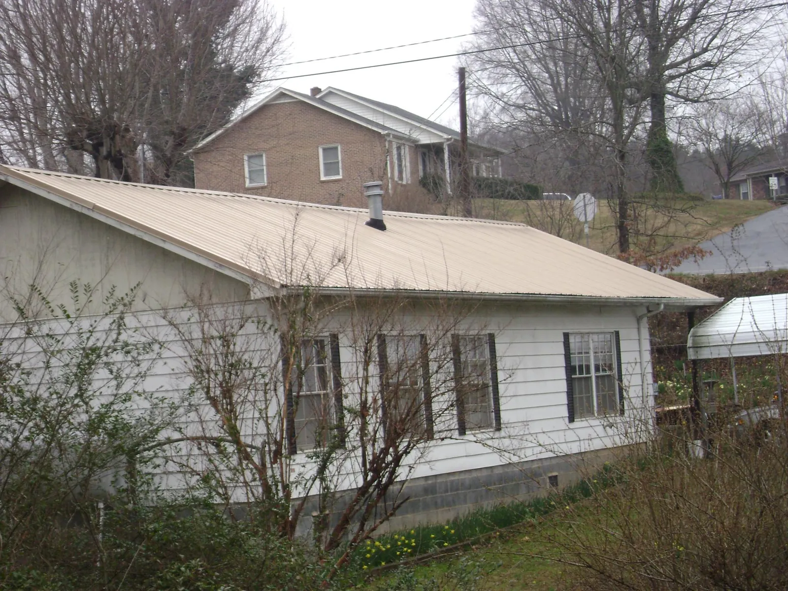 Tan metal roof on a white sided house set into a hillside — Commercial Roofing by Roofing Brothers in Independence